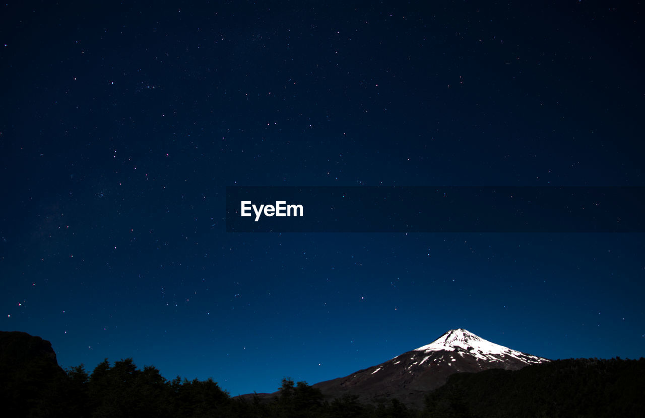 Low angle scenic view of star field over mountain against blue sky during winter