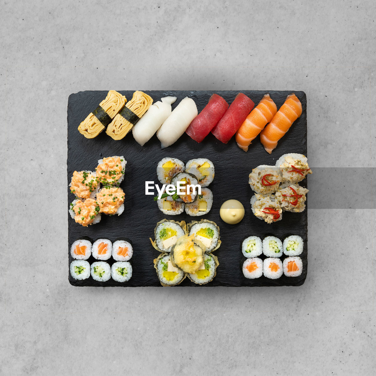 Big set of sushi and maki rolls on special black plate at grey stone table