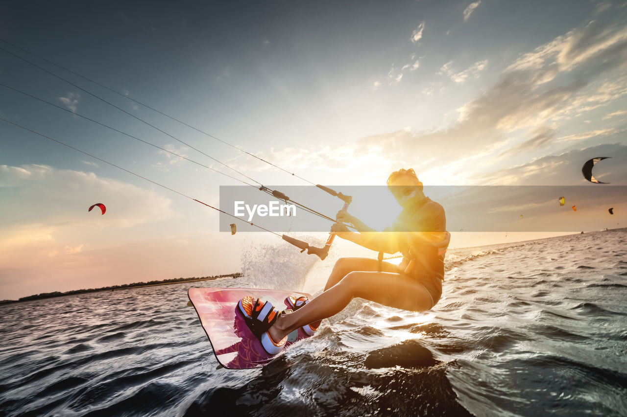 Woman kitesurfing against sky during sunset