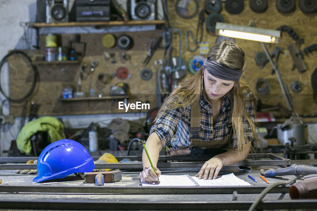 Woman writing in book while standing against work tools