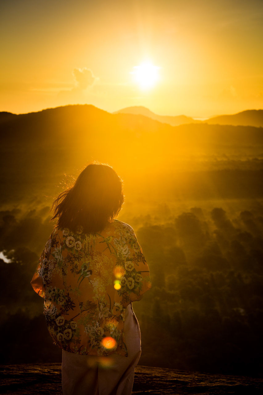 Rear view of woman standing on mountain during sunset