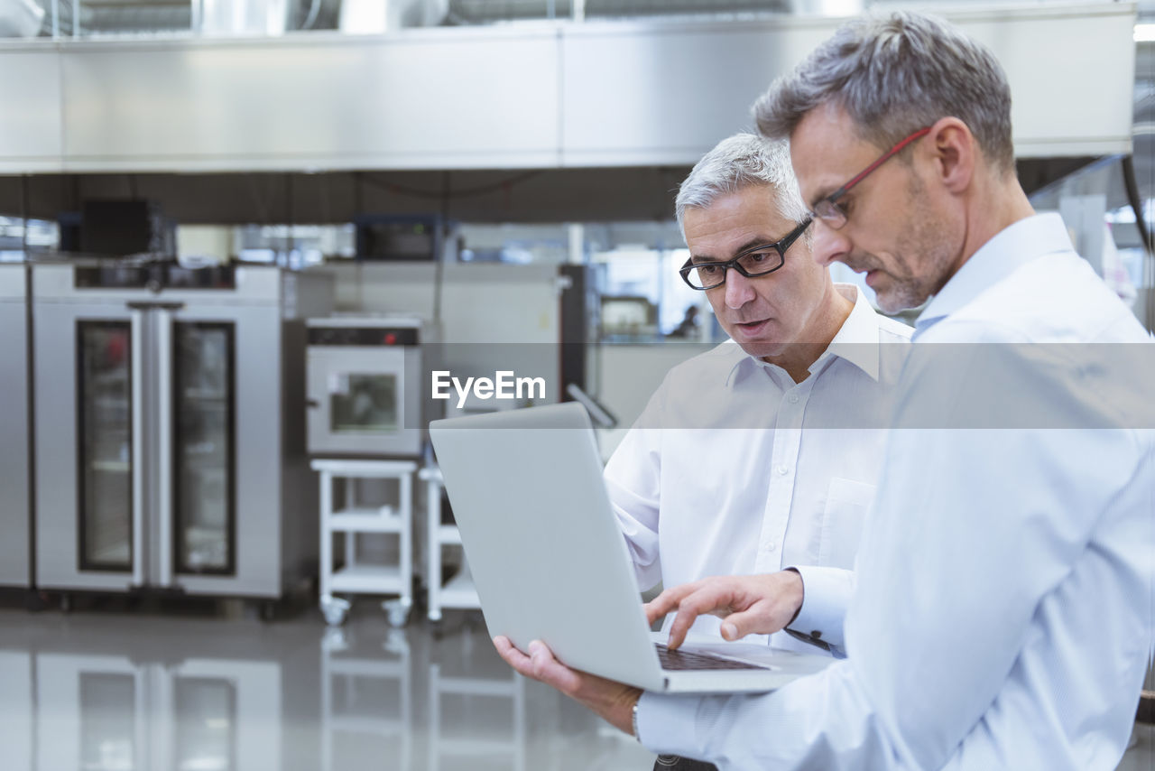 Two managers standing in company using laptop