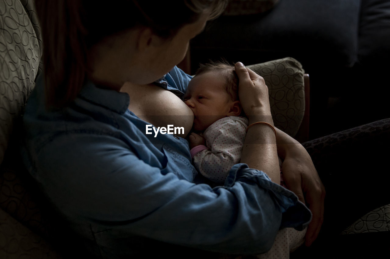 High angle view of mother breastfeeding newborn daughter while sitting on sofa at home