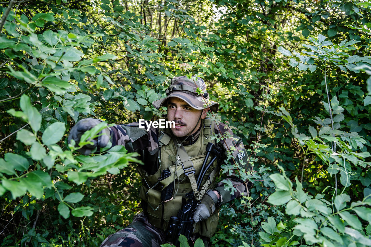 Soldier holding gun while hiding amidst plants