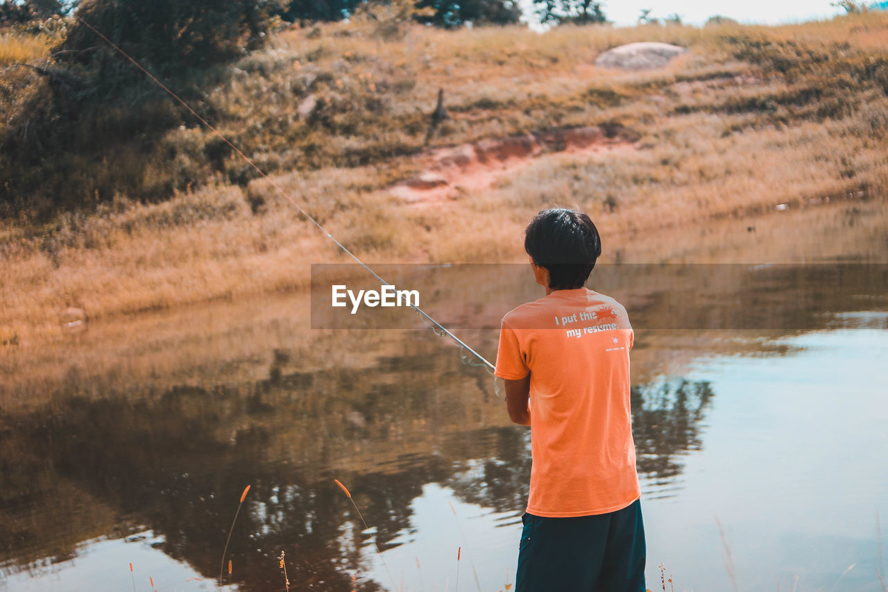 REAR VIEW OF A BOY FISHING IN LAKE