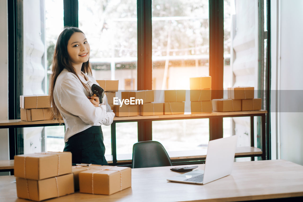 Portrait of young businesswoman standing by packages at office