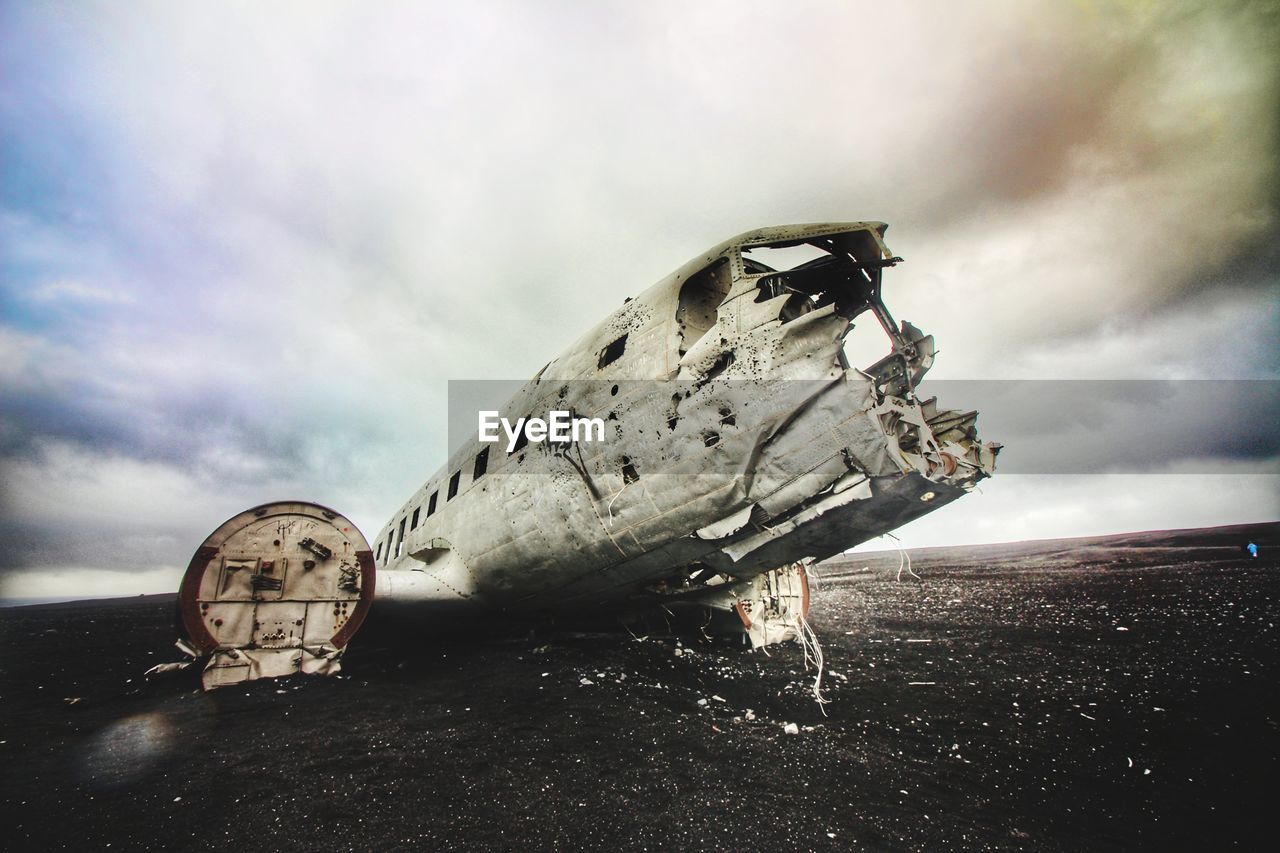 Abandoned airplane on beach against cloudy sky