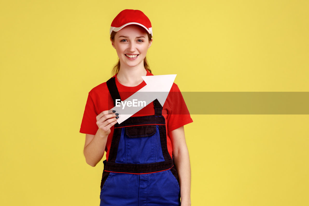 portrait of smiling young woman holding box against yellow background