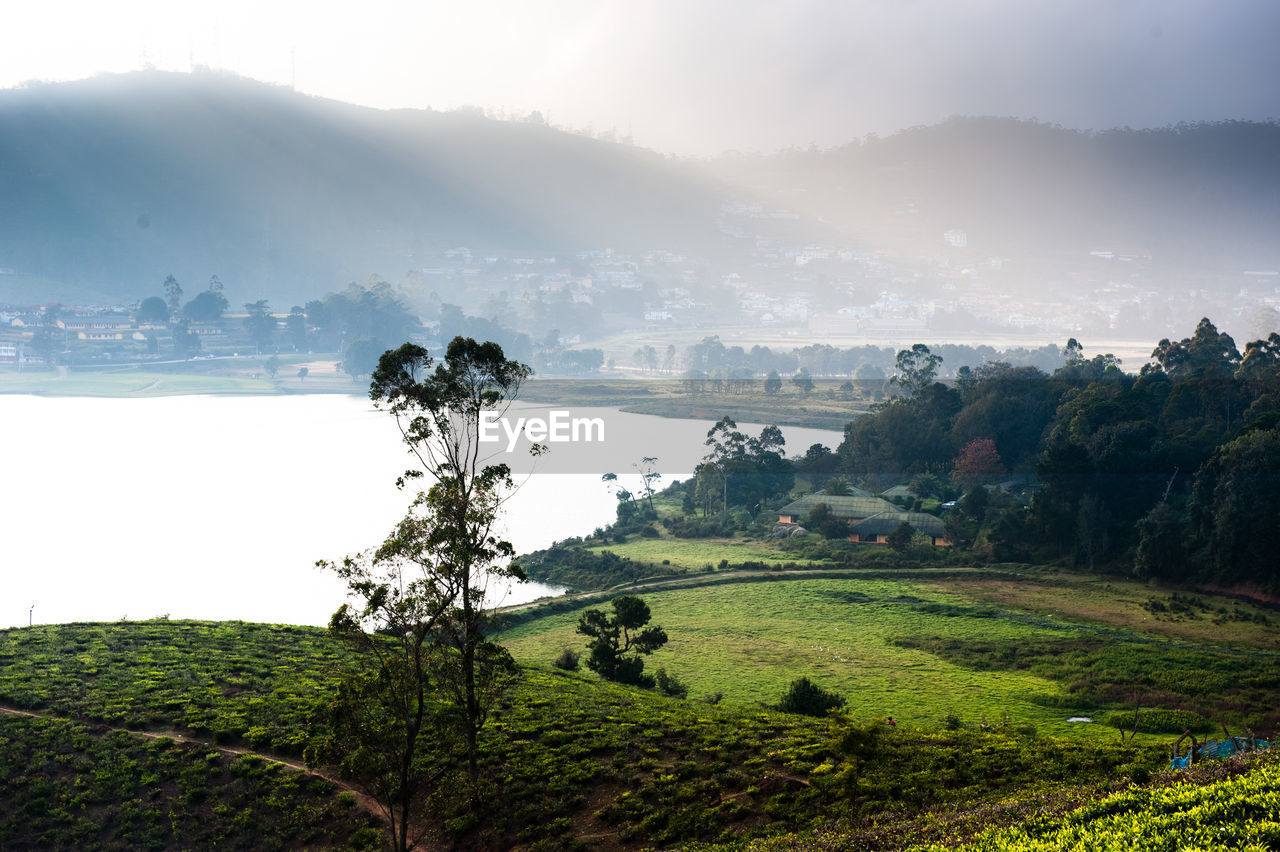 Scenic view of lake by mountains during foggy weather