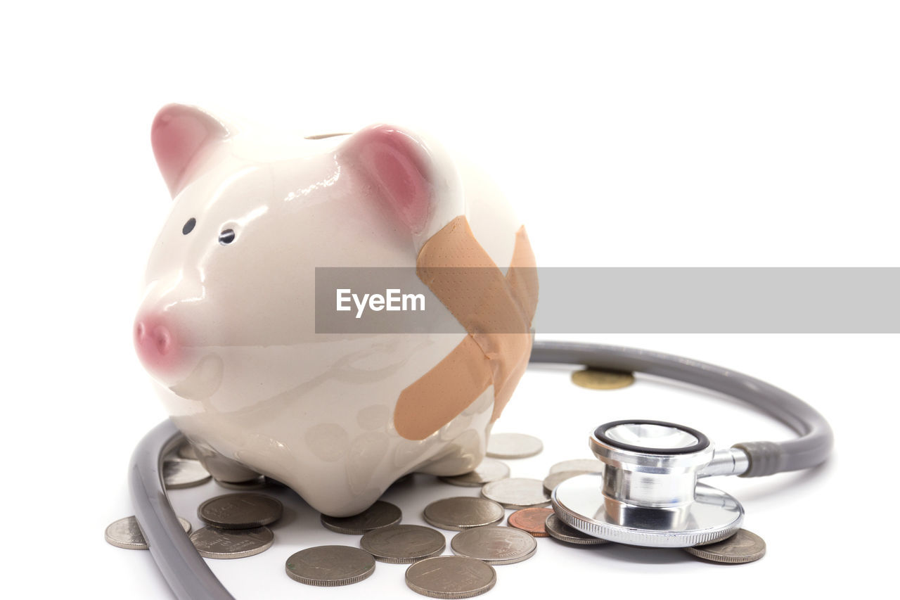 Close-up of piggy bank with stethoscope against white background