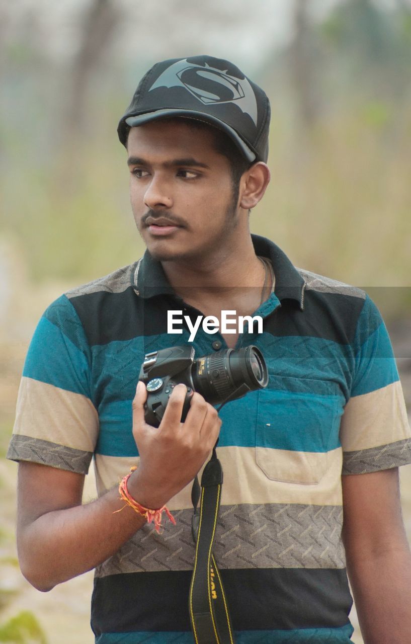 PORTRAIT OF YOUNG MAN HOLDING CAMERA