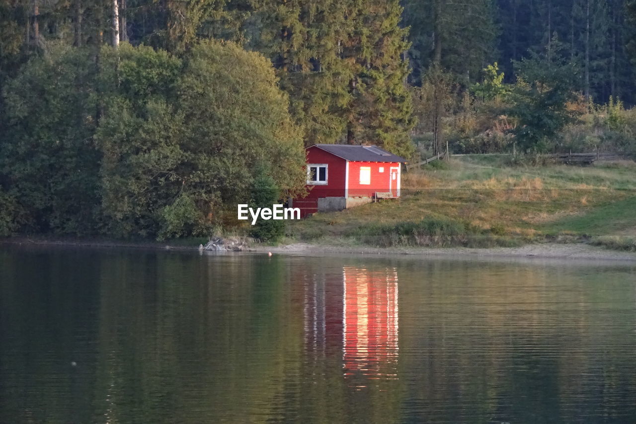 VIEW OF COTTAGE BY LAKE AGAINST TREES IN FOREST