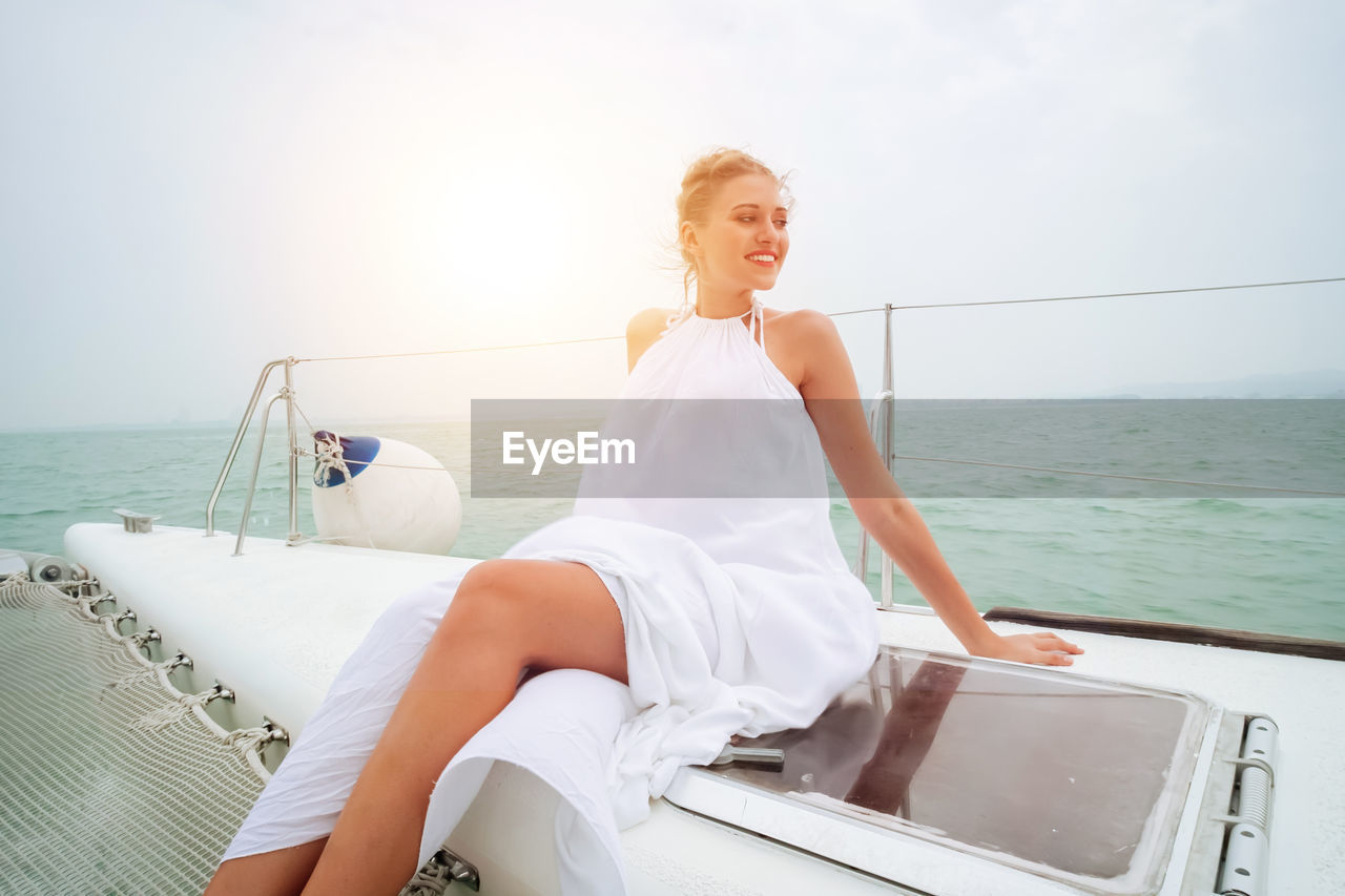 YOUNG WOMAN SITTING ON BOAT AGAINST SEA