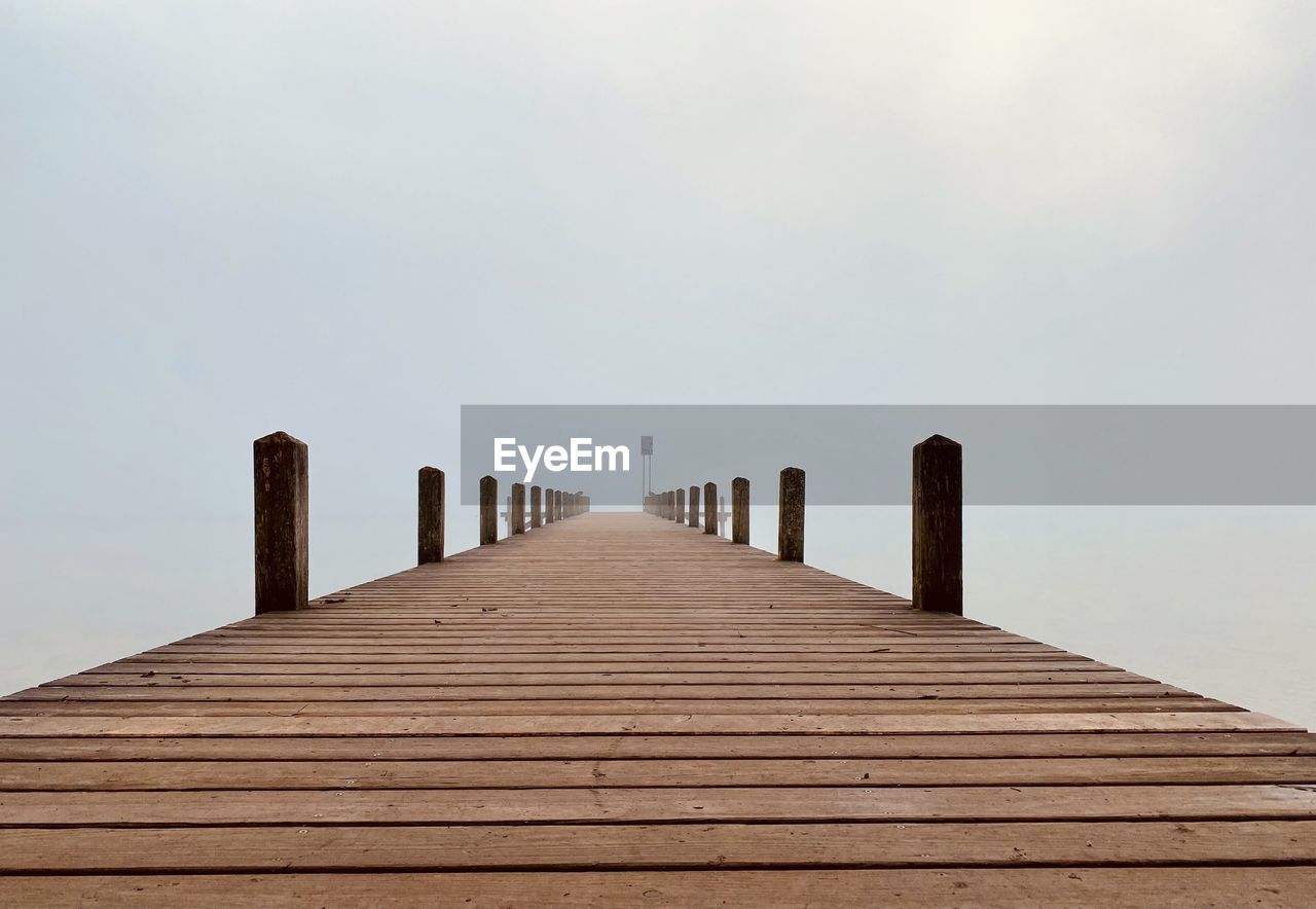 Wooden jetty leading to sea against clear sky