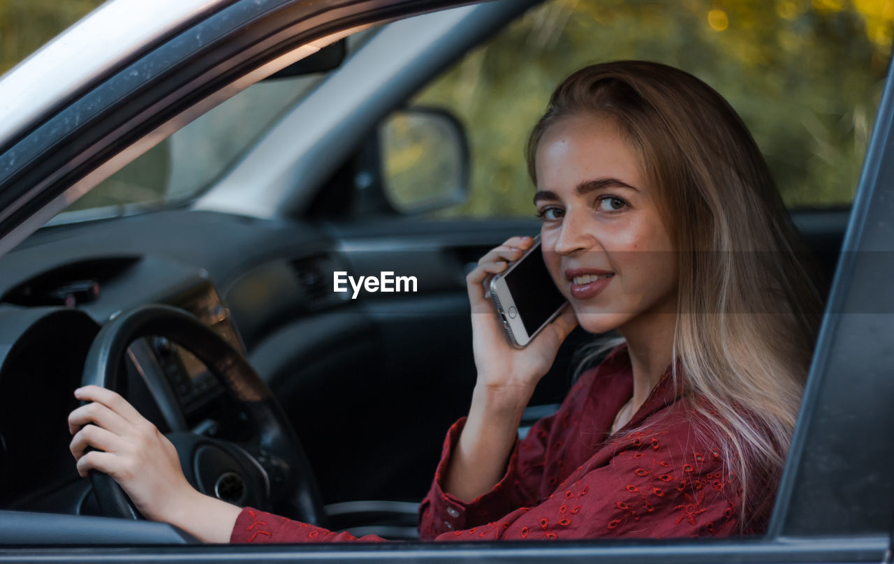 YOUNG WOMAN USING SMART PHONE WHILE SITTING IN CAR