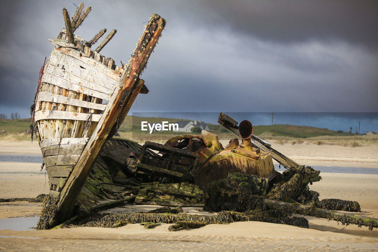 vehicle, sea, shipwreck, transportation, nautical vessel, beach, ship, water, land, abandoned, nature, coast, mode of transportation, sky, cloud, sand, ruined, damaged, history, destruction, ocean, outdoors, watercraft, sinking, deterioration, decline, boat, no people, day, environment, the past, rundown