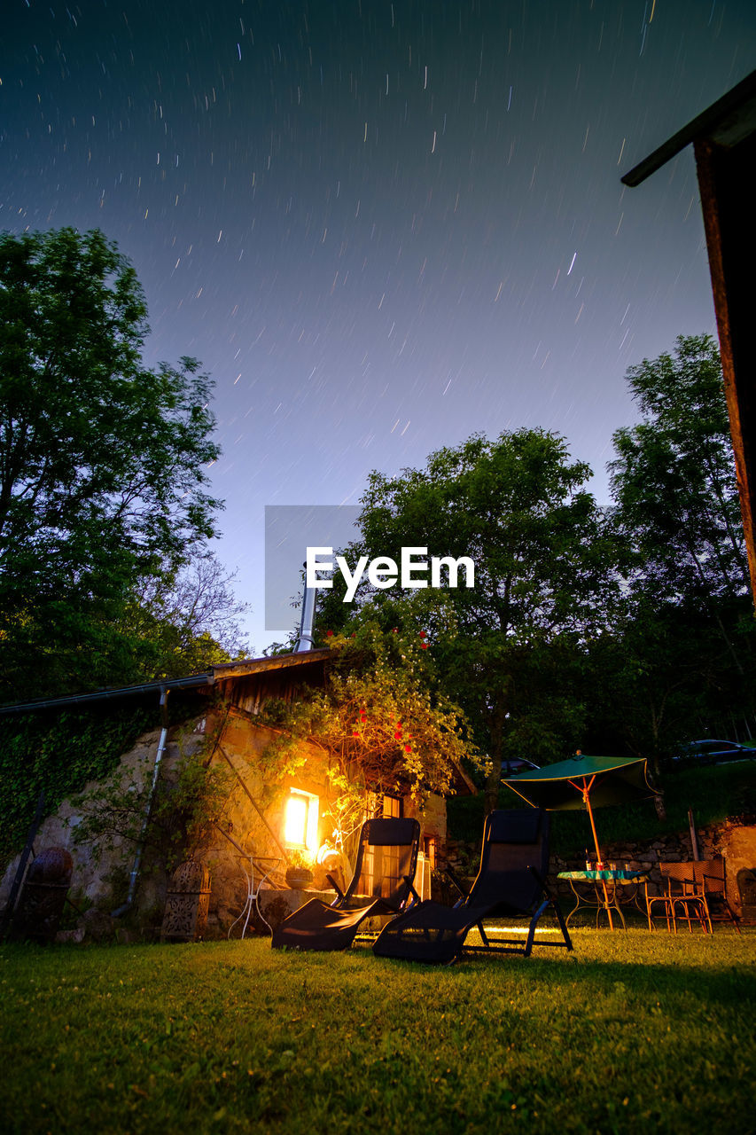 Chairs by illuminated house against starry sky at night