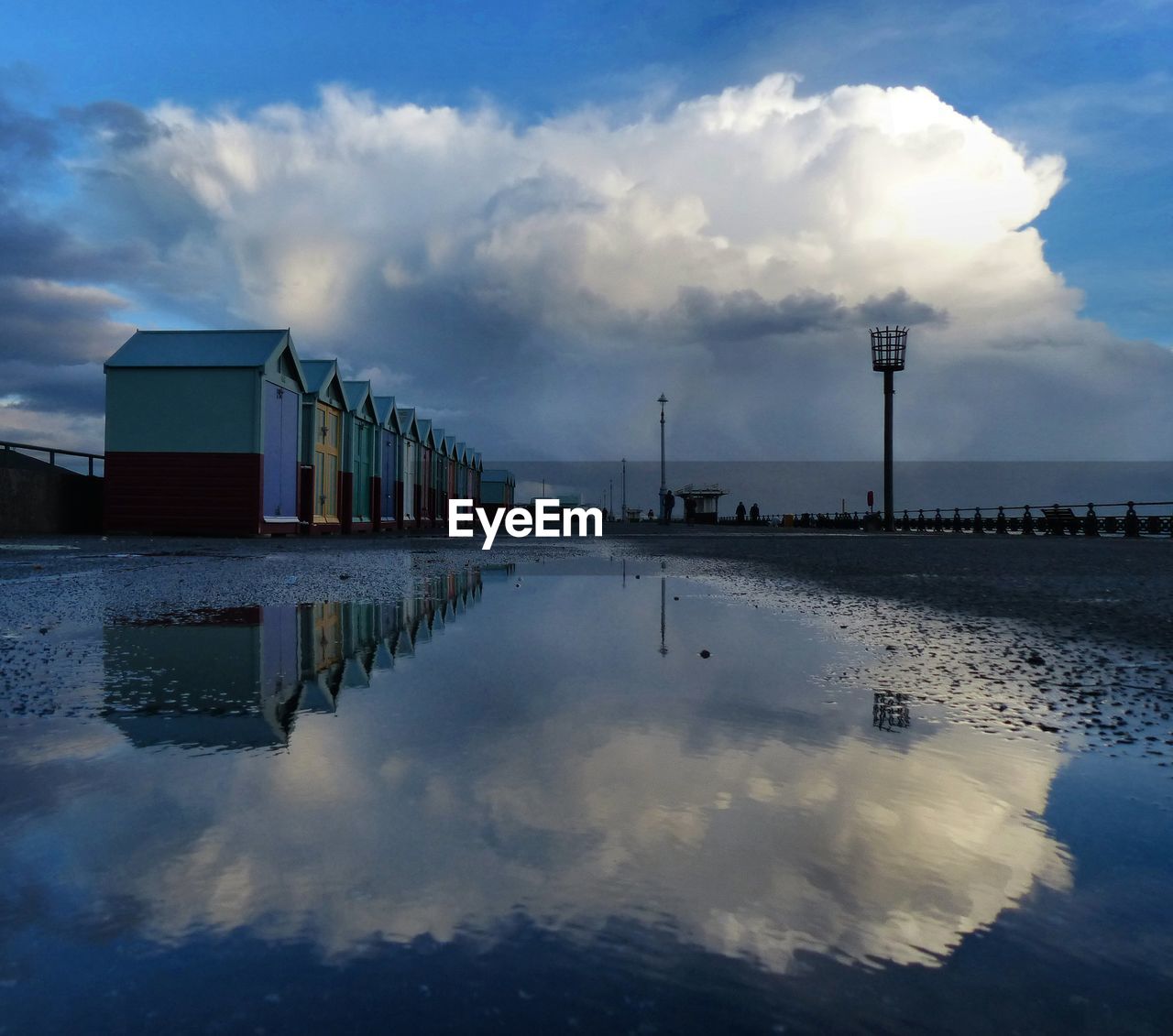 Sky reflecting on puddle by beach huts