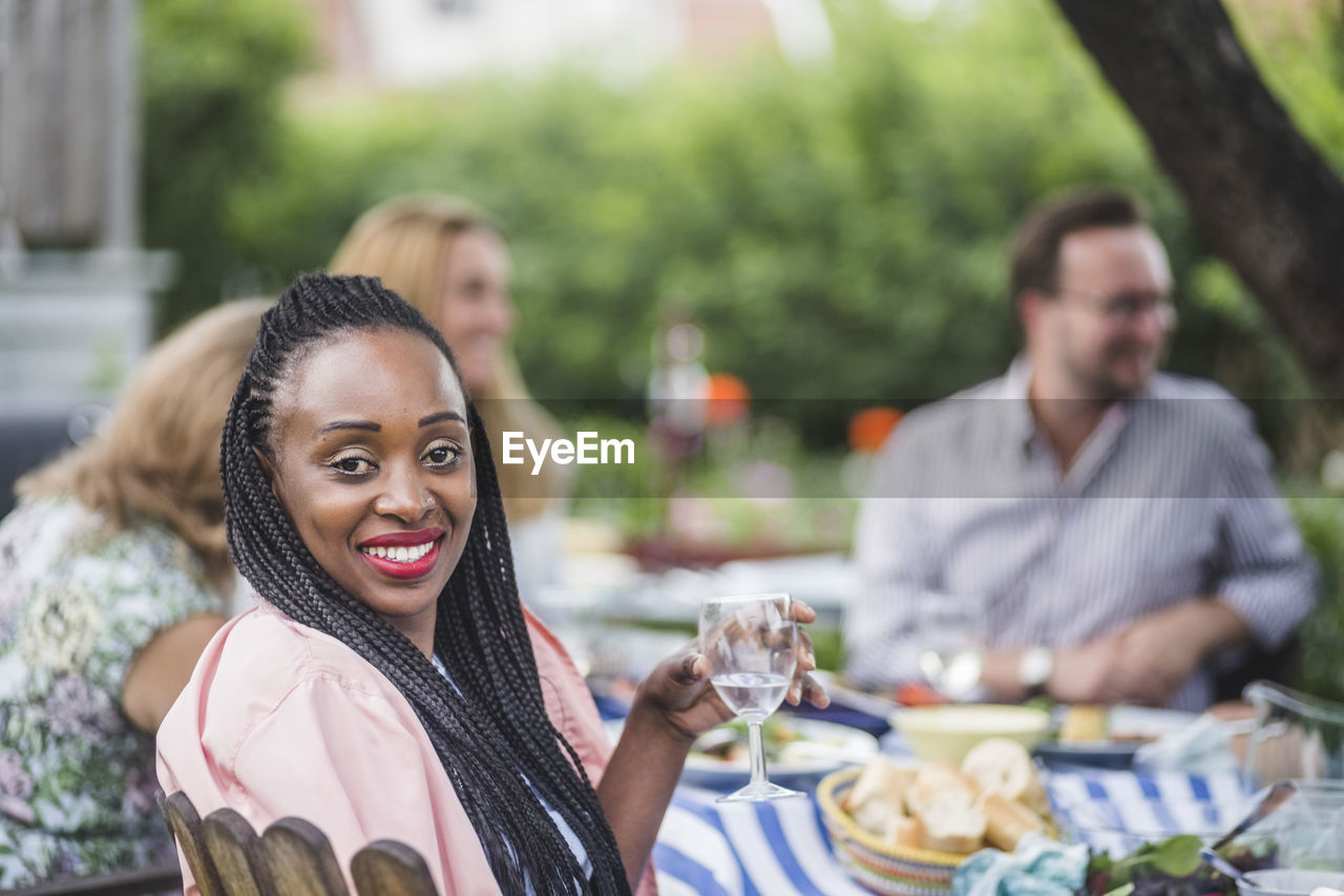Portrait of smiling woman having wine while sitting with friends at garden party
