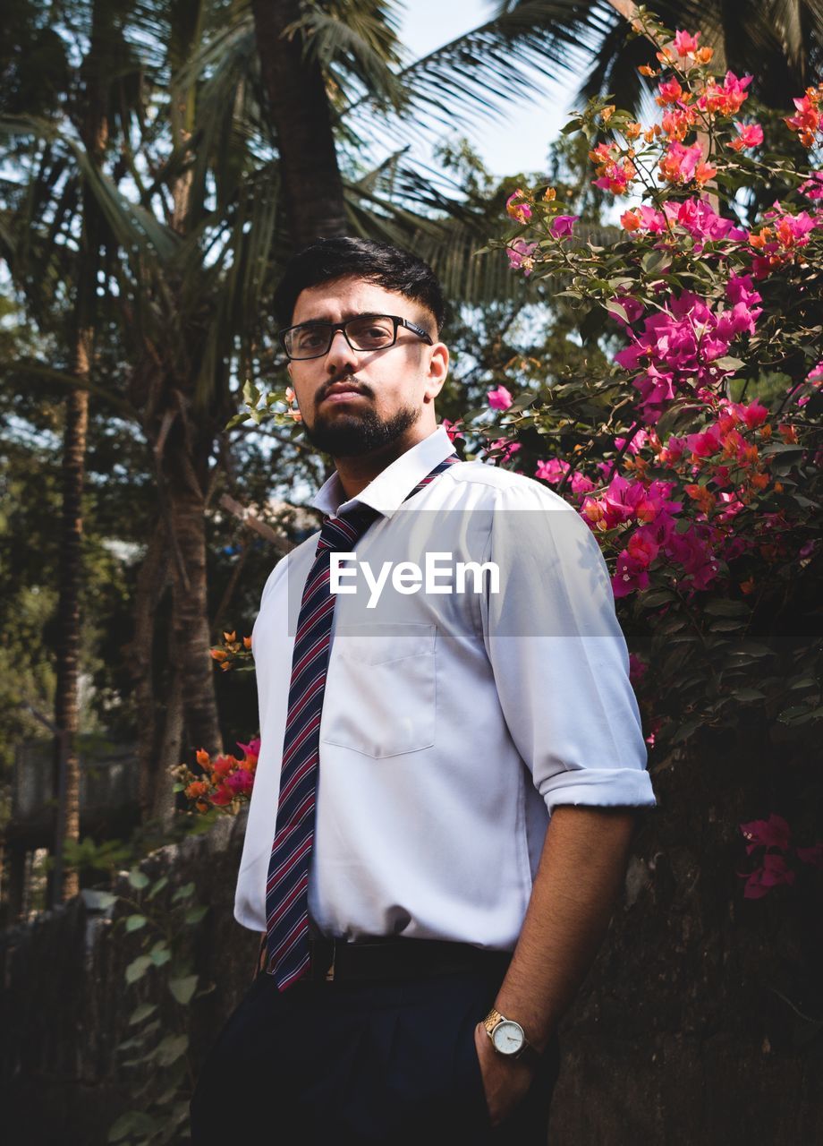 Portrait of young man wearing eyeglasses while standing against plants