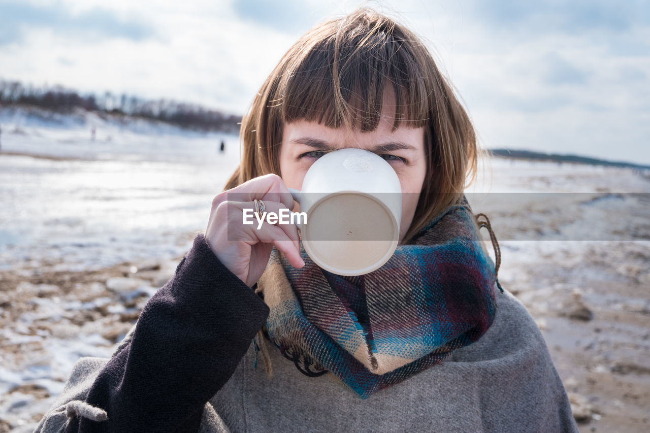 Close-up portrait of young woman drinking coffee at beach