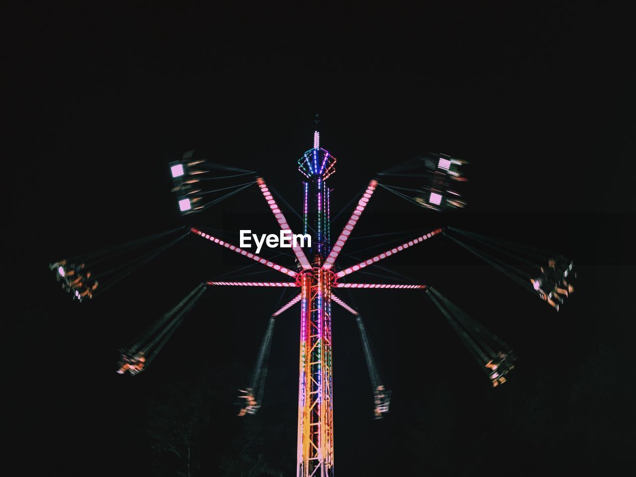 Low angle view of people enjoying illuminated chain swing ride against sky at night