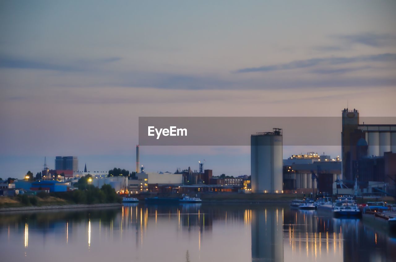 Boats moored in illuminated city against sky during sunset