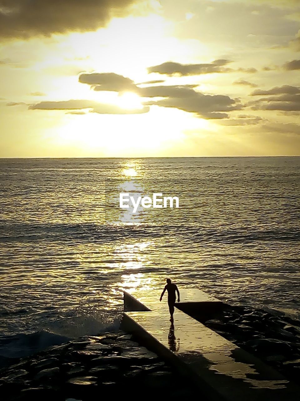 SILHOUETTE MAN STANDING AT SEA SHORE AGAINST SKY DURING SUNSET