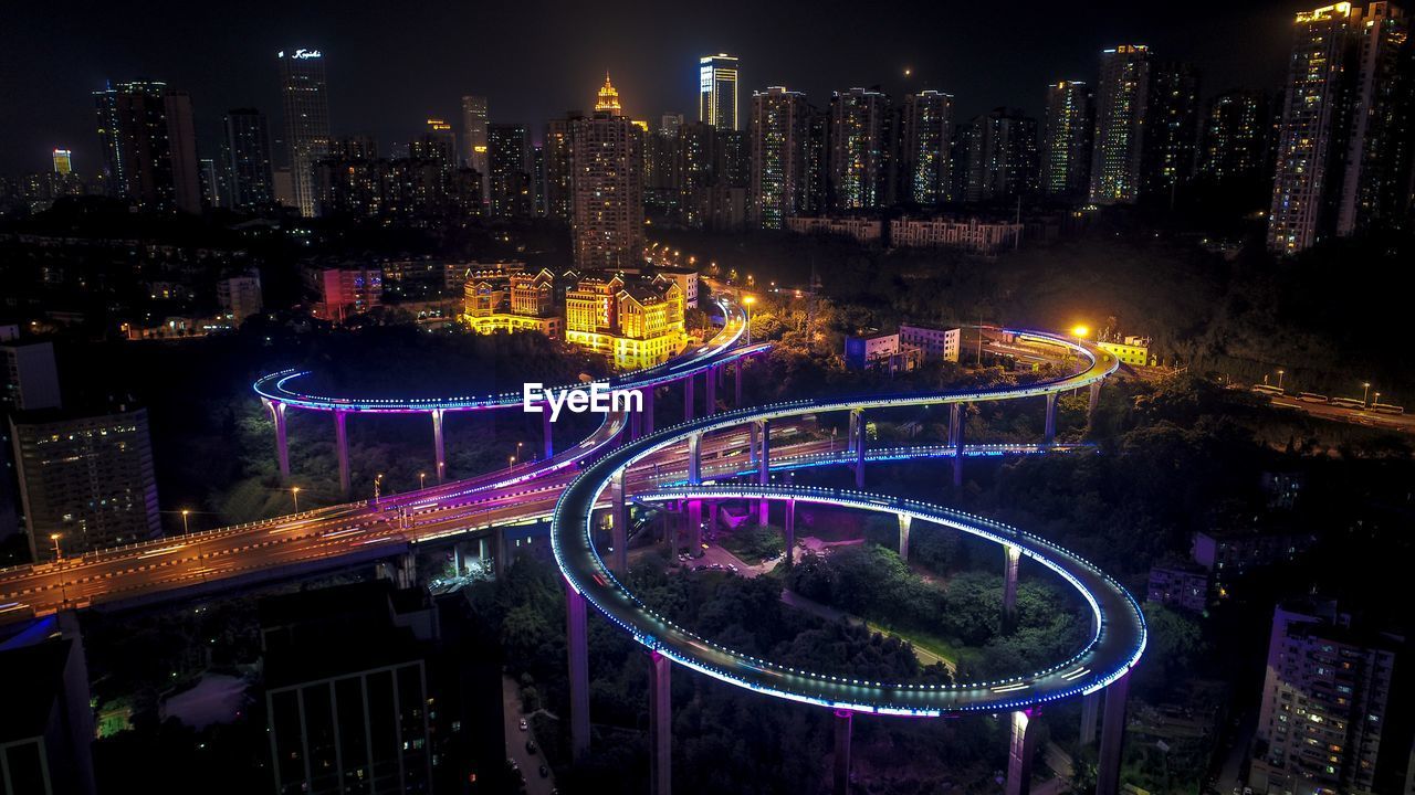 Aerial view of illuminated elevated road by buildings at night