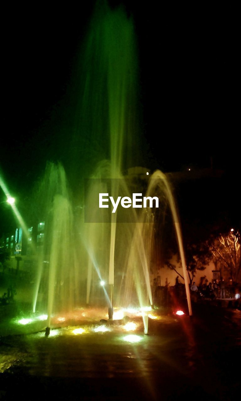 Illuminated fountains in garden against clear sky at night