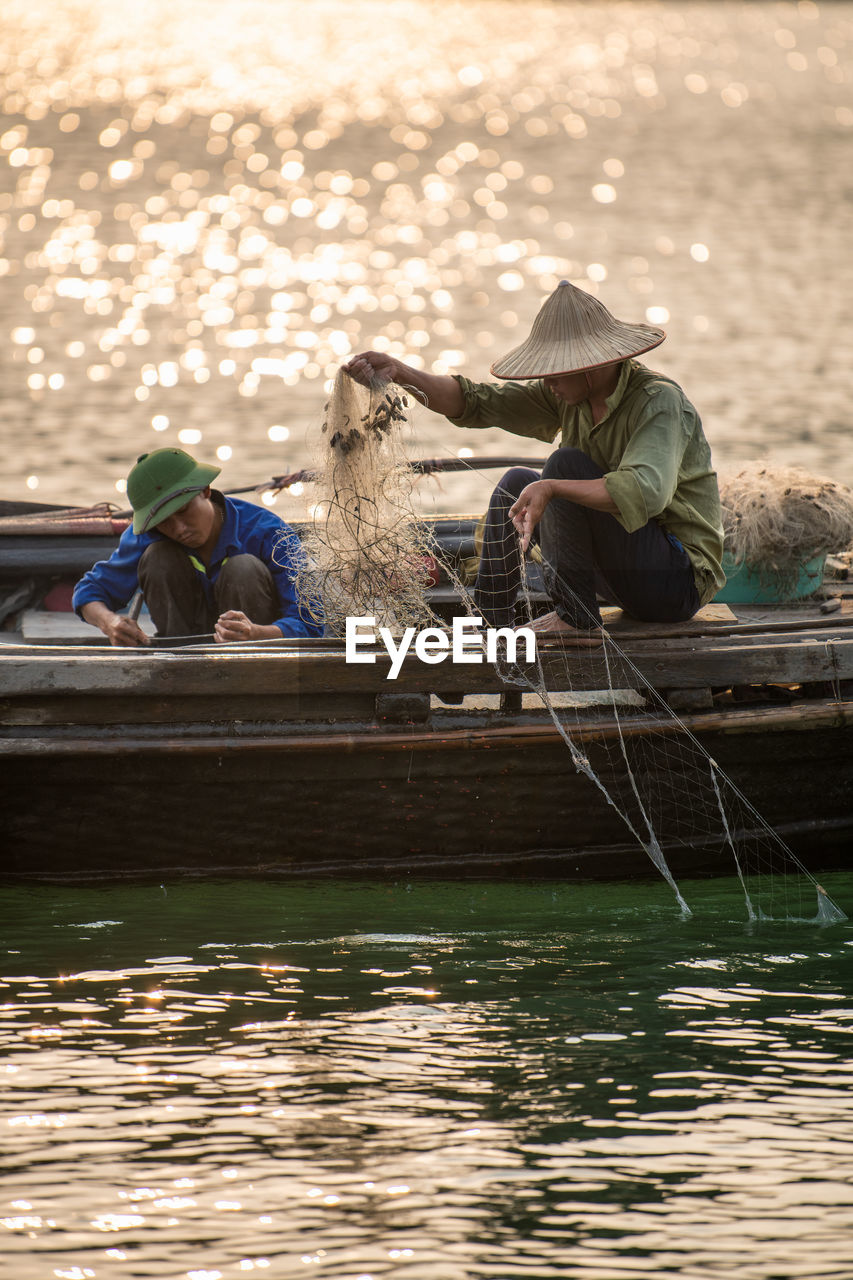 Fishermen placing fishing net on boat at lake