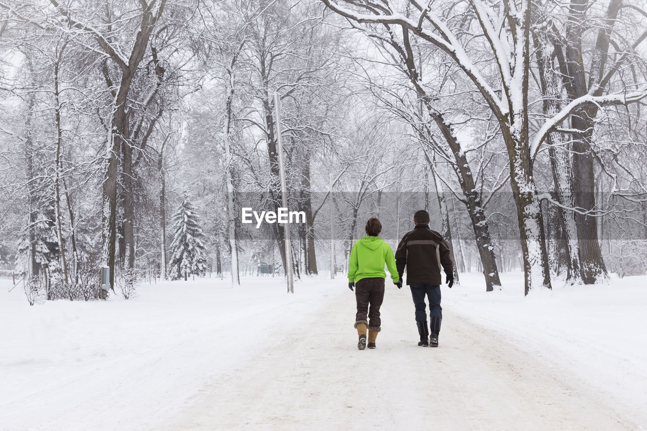 REAR VIEW OF MEN WALKING ON SNOW COVERED TREES