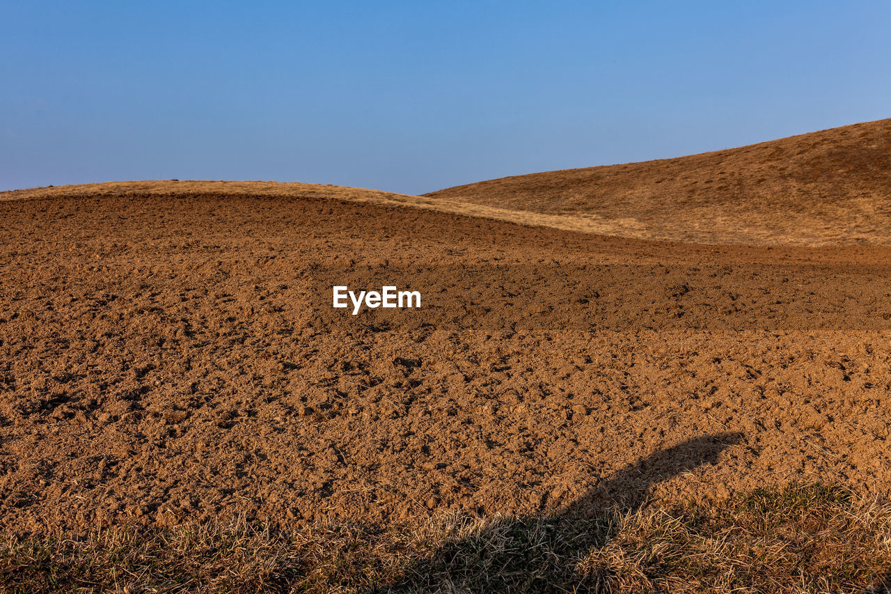 Plowed red earth fields on the background of the blue sky with a shadow in the foreground