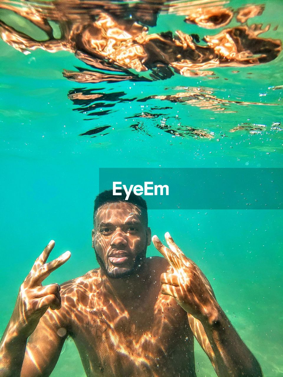 Portrait of shirtless man gesturing while swimming in sea