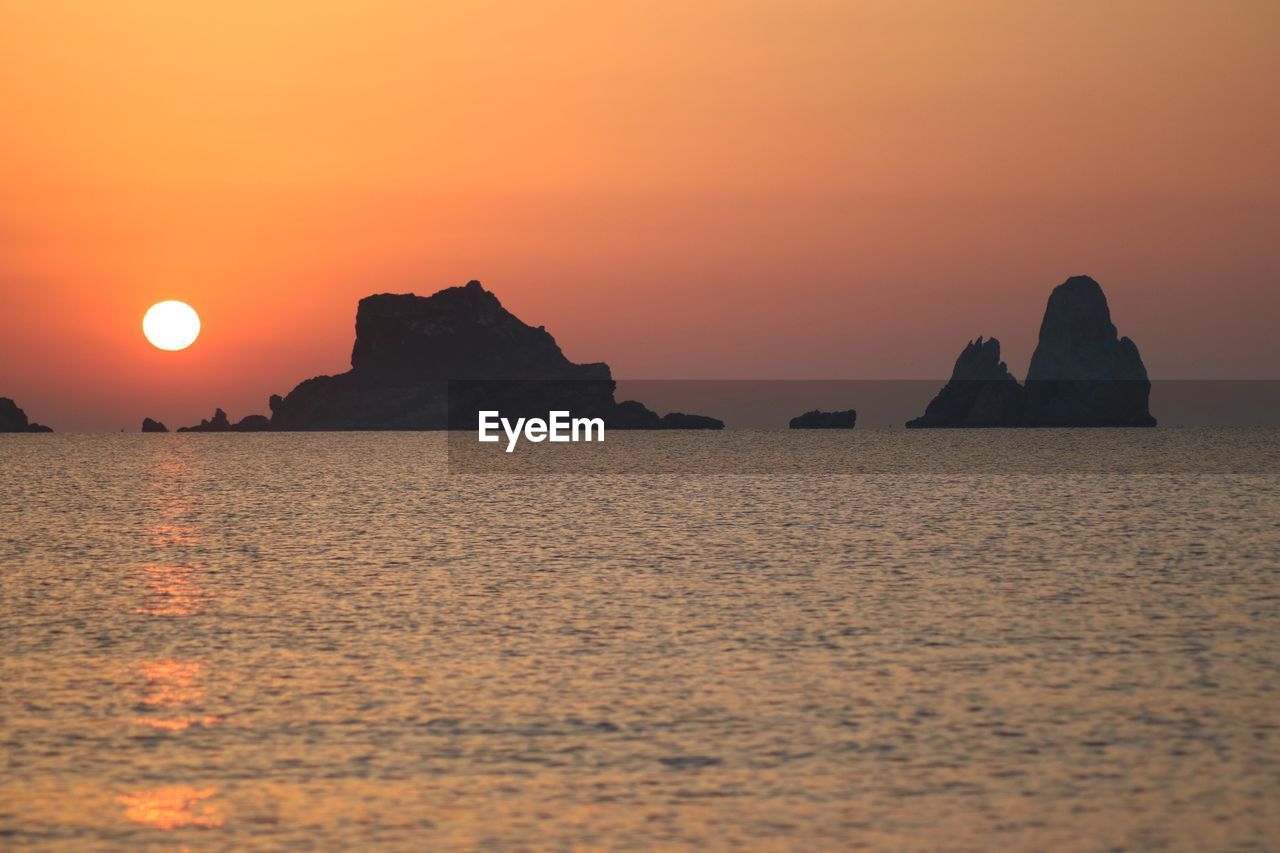 SCENIC VIEW OF ROCK FORMATION IN SEA AGAINST ORANGE SKY