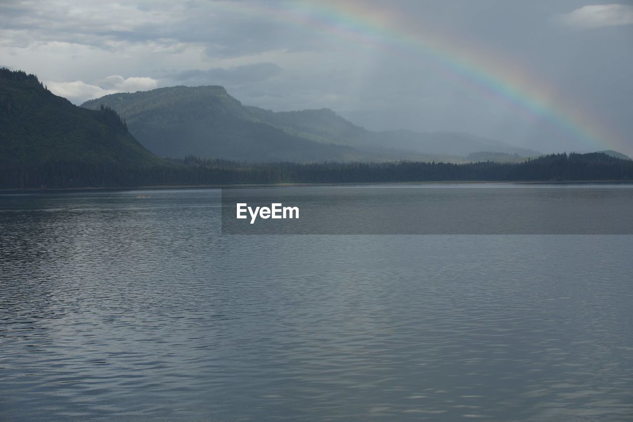 SCENIC VIEW OF RAINBOW OVER LAKE AGAINST MOUNTAINS