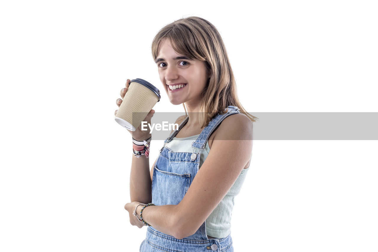 one person, white background, women, smiling, casual clothing, portrait, happiness, cut out, adult, studio shot, drink, emotion, food and drink, young adult, refreshment, indoors, drinking, lifestyles, holding, person, female, looking at camera, finger, child, standing, blond hair, clothing, hand, cheerful, relaxation, copy space, hairstyle, waist up, teeth, smile, arm, enjoyment, positive emotion, long hair, jeans, cute, side view, three quarter length, denim, cup, teenager, looking, childhood, human face