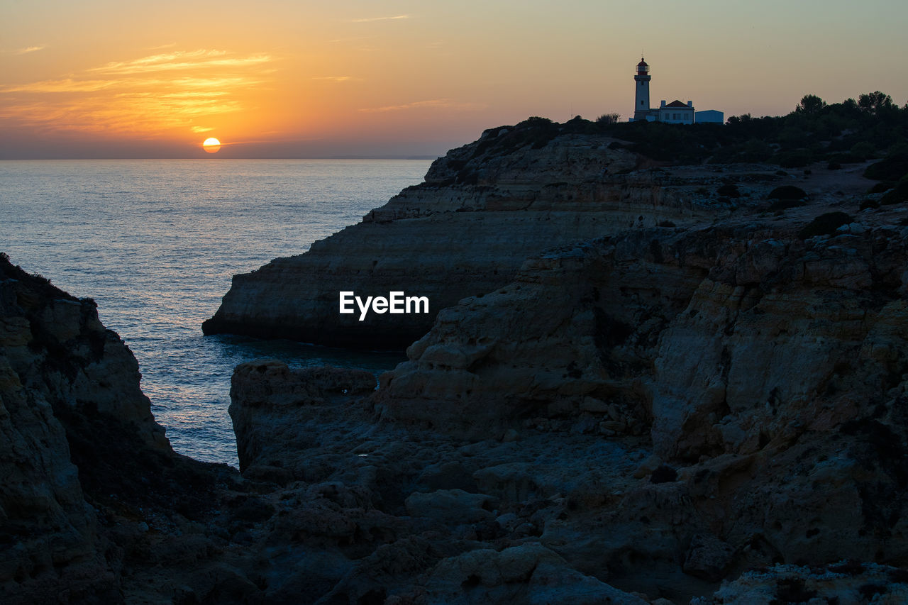 Rock formations on shore against sky during sunset