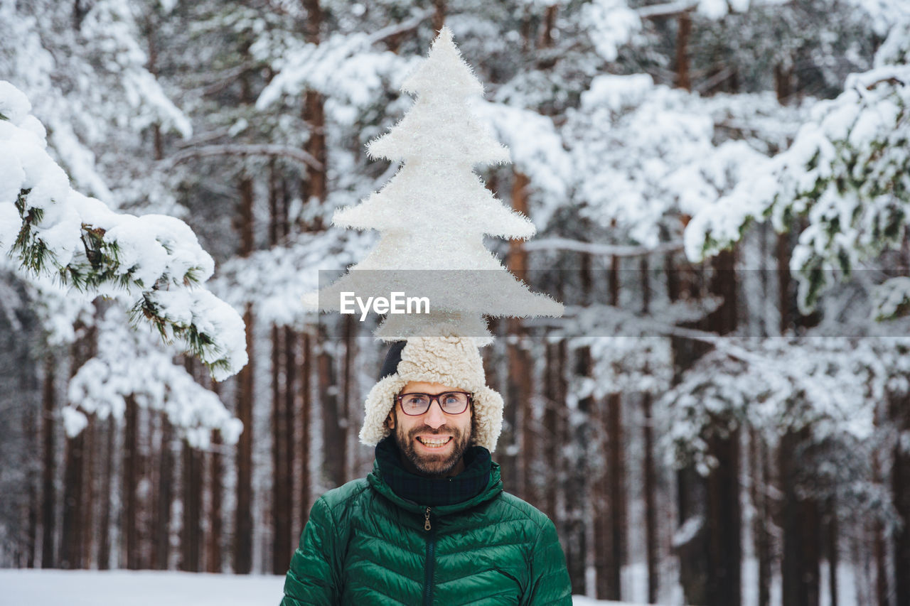 PORTRAIT OF SMILING YOUNG WOMAN STANDING ON SNOW COVERED TREES