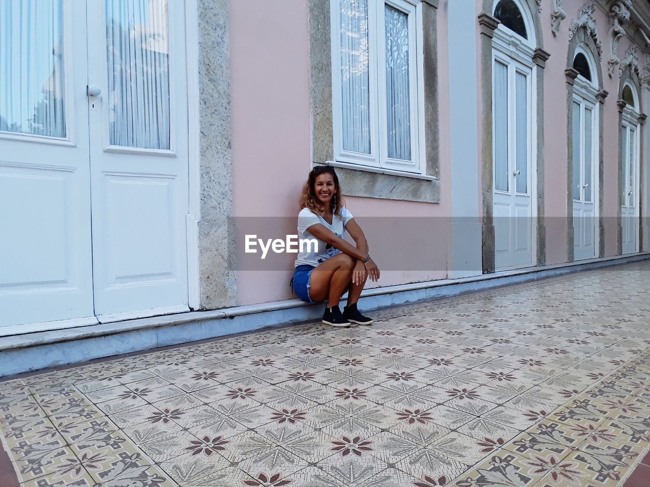 PORTRAIT OF YOUNG WOMAN SITTING ON BUILDING