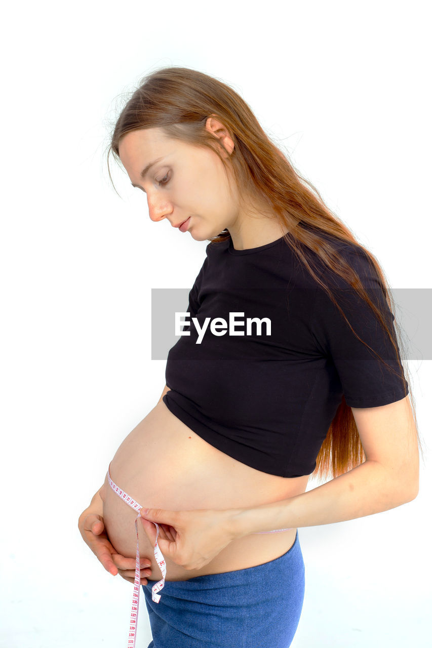 women, adult, one person, pregnant, studio shot, trunk, female, arm, parent, anticipation, clothing, young adult, indoors, limb, side view, beginnings, white background, lifestyles, human leg, standing, emotion, human fertility, smiling, finger, three quarter length, hands on stomach, positive emotion, touching, hairstyle, hand, wellbeing, casual clothing, happiness, person, long hair, undergarment, photo shoot, looking, portrait, cut out, child, prenatal care, dieting, waist up, vitality, relaxation, sleeve, blond hair, holding, hope