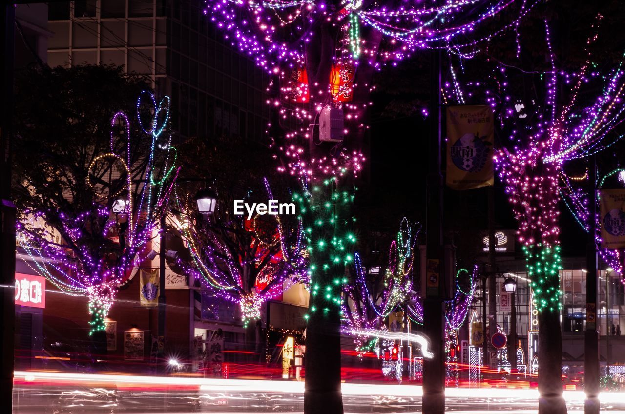 Light trails amidst illuminated trees in city during christmas