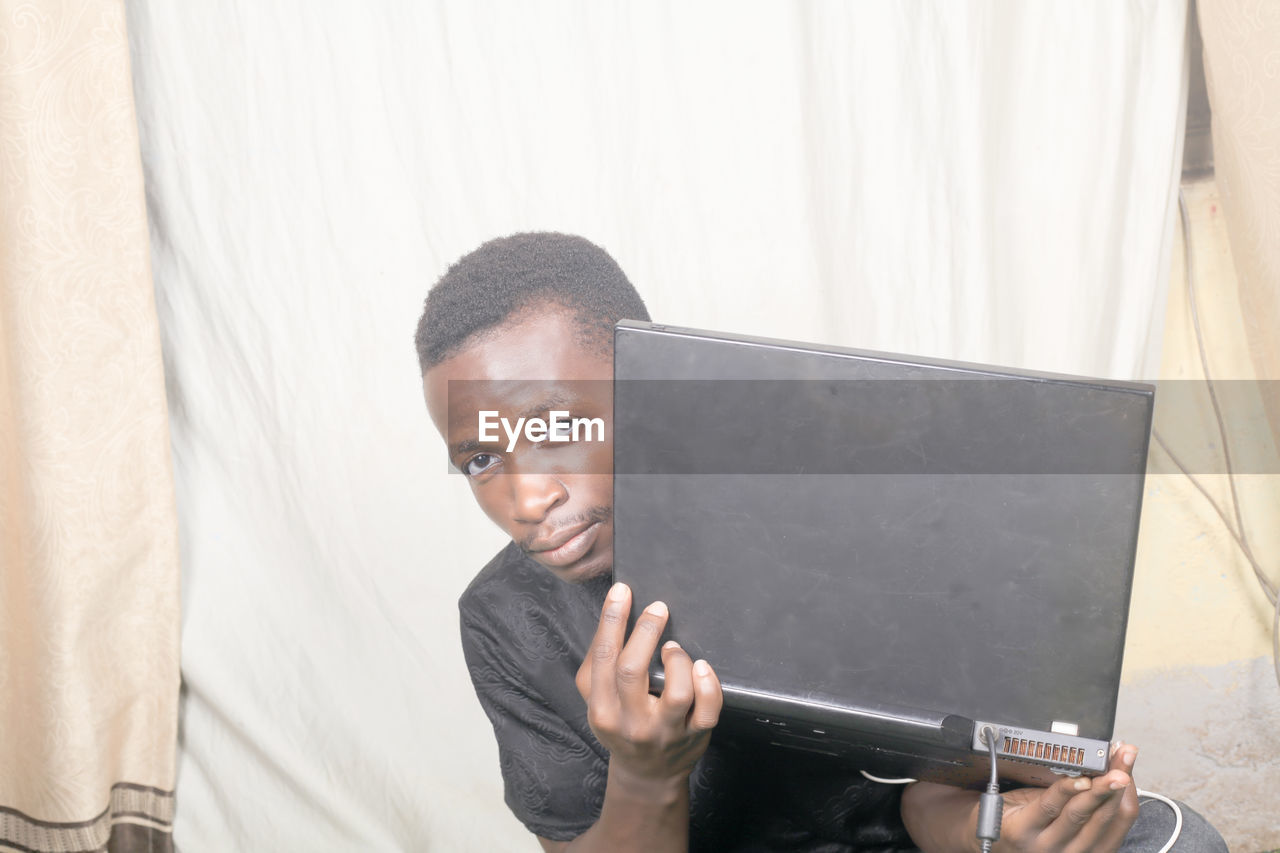 PORTRAIT OF MATURE MAN HOLDING CAMERA WHILE STANDING AGAINST CURTAIN