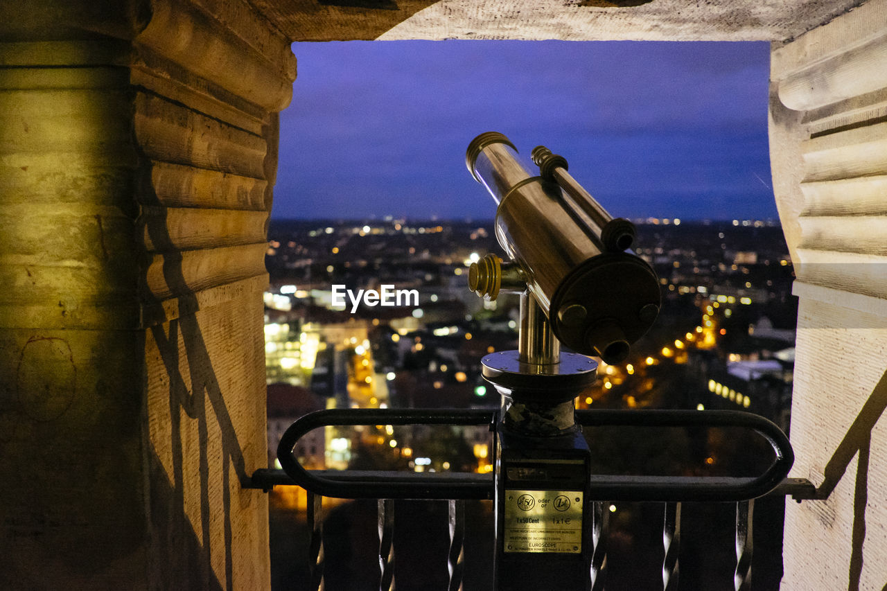 Coin-operated binoculars against illuminated cityscape at night