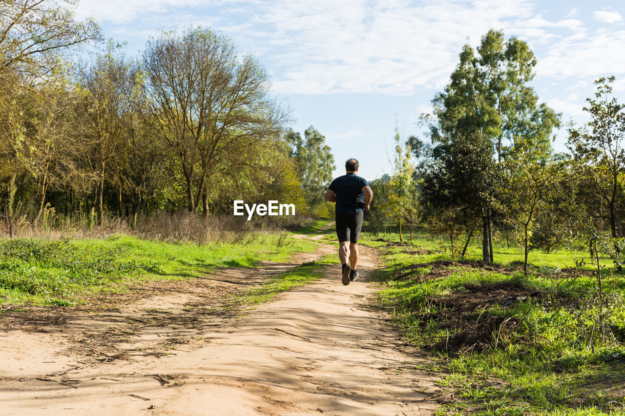 Rear view of man running on footpath against sky