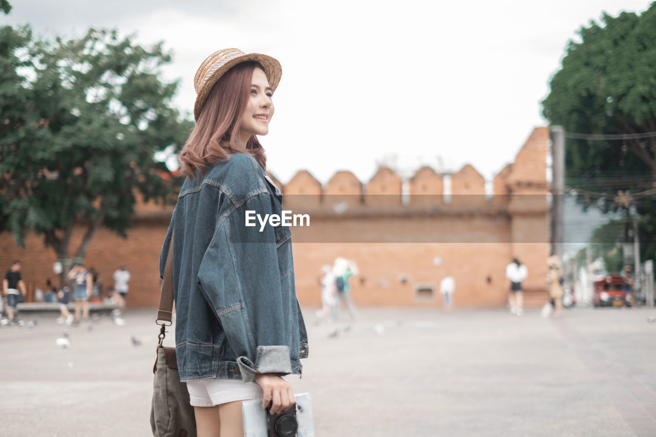 YOUNG WOMAN STANDING AGAINST CITY