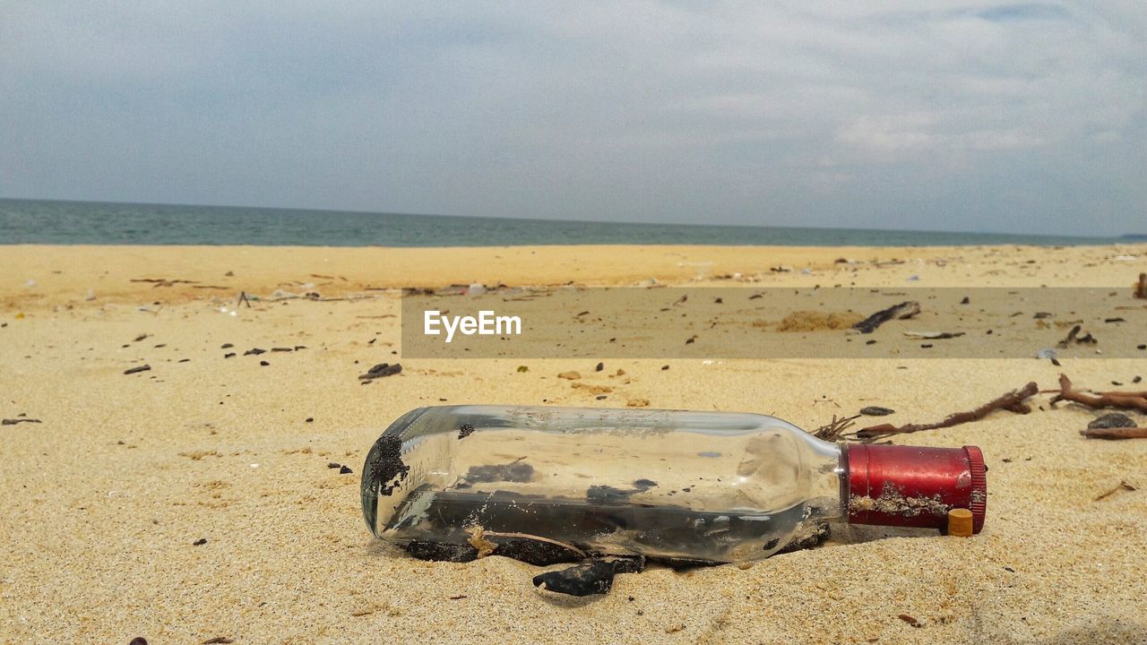 CLOSE-UP OF BOTTLE ON SHORE AT BEACH