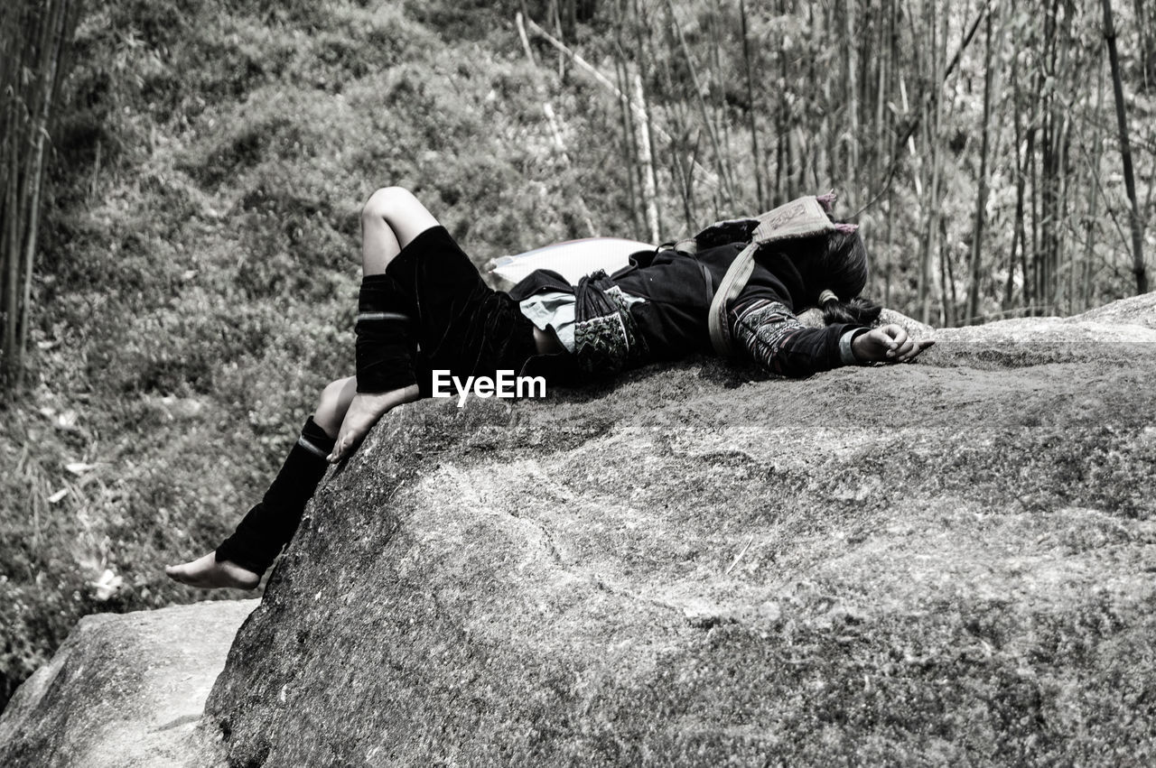 Woman sleeping on rock against trees in forest