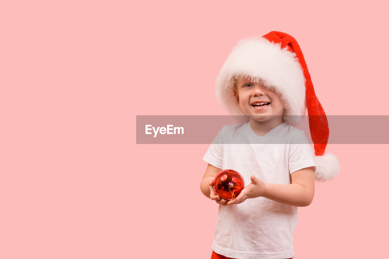 Boy child toddler kid 3 years old in a hat of santa claus stands and holds a new year's ball. 