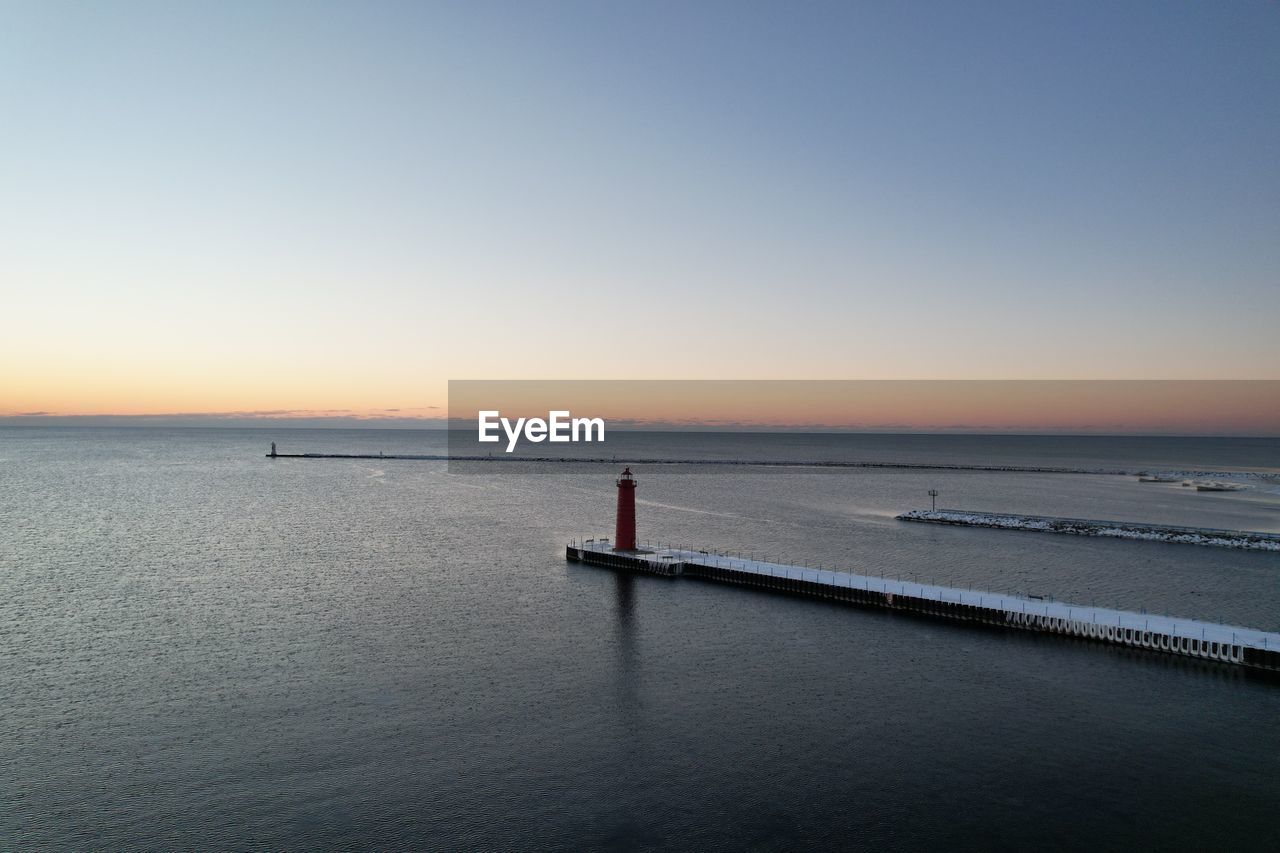 water, sea, sky, horizon, scenics - nature, horizon over water, beauty in nature, dawn, tranquility, shore, beach, nature, sunset, ocean, land, tranquil scene, clear sky, body of water, reflection, coast, copy space, idyllic, wave, blue, travel, holiday, architecture, outdoors, bay, travel destinations, vacation, non-urban scene, trip, one person, transportation, seascape, silhouette, breakwater, environment, built structure, nautical vessel, urban skyline, pier, sunlight, landscape, day